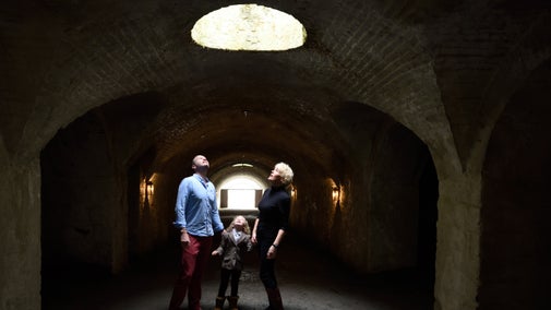 A man, woman and child in a dark tunnel looking up at a light coming through a hole in the ceiling